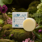 Bar of soap and packaging labeled 'Clean Locks' on a mossy surface with flowers in the background Bar of soap and packaging labeled 'Clean Locks' on a mossy surface with flowers in the background