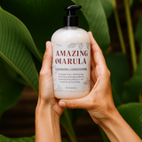 Hand holding a bottle of 'Amazing Marula' cleansing conditioner with green leaves in the background Hand holding a bottle of 'Amazing Marula' cleansing conditioner with green leaves in the background
