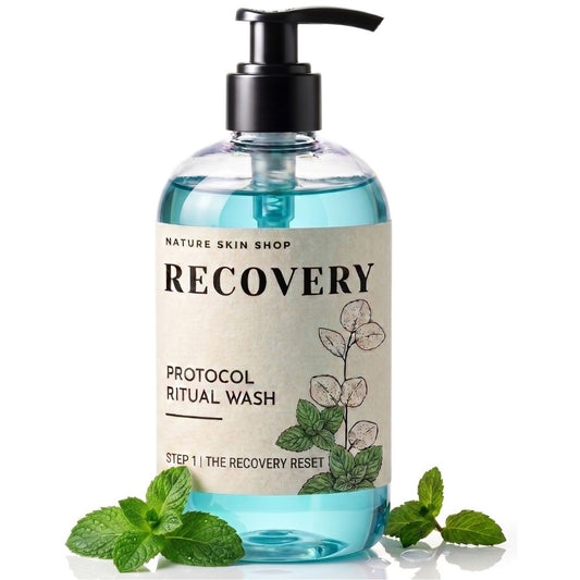A bottle of Nature Skin Shop Recovery Protocol Ritual Wash with a black pump, clear bottle showing blue liquid, and a beige label with botanical illustrations, styled with mint leaves on a white background.
