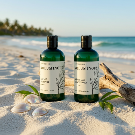 Two bottles of Voluminous hair care products on a sandy beach with ocean and palm trees in the background.