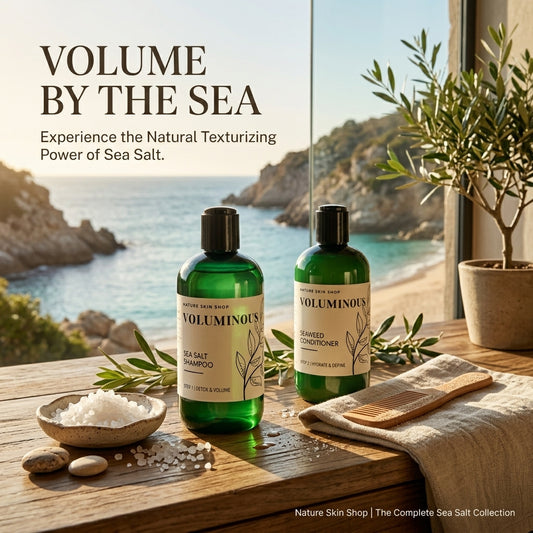 Two green bottles of Volumnous hair care products, Sea Salt Shampoo and Seaweed Conditioner, displayed on a wooden table with a beach background. The scene includes a small bowl of sea salt, a wooden brush, and a potted olive tree.