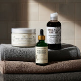 Set of hair care products including shampoo, conditioner, and serum on towels with a tiled wall background.