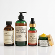 A five-piece skincare set from Nature Skin Shop arranged on a reflective white surface. The set includes an amber glass bottle of Skin Balancing Toner, a green glass pump bottle of Ancestral Rice Milk & Manjistha Facial Cleanser, an amber glass dropper bottle of Skin Glow Astaxanthin Serum with a gold collar, and a green jar of Turmeric Glow nourishing jelly face cream with its gold lid leaning against it.