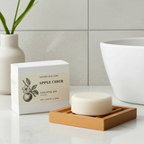 Bar of soap on a wooden dish with packaging labeled 'Apple Cider' in a bathroom setting.