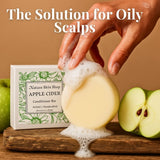 Bar of soap with foam, hand holding it, and 'Nature Skin Shop Apple Cider' conditioner bar with apples on a wooden surface.