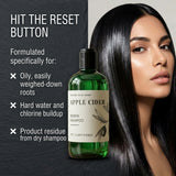 A bottle of Nature Skin Shop Apple Cider Renew Shampoo is shown next to a model with long, shiny black hair. The left side features a dark slate background with promotional text about clearing product residue and oily roots.
