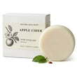 An apple cider shine ritual bar soap next to its white packaging box by Nature Skin Shop, with green leaves and a small seed prop on a white background.