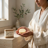 Person holding a bar of soap with a box labeled 'Apple Cider Vinegar' in a serene bathroom setting.