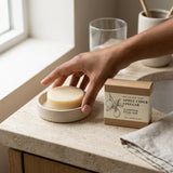Hand reaching for a bar of soap on a stone surface with a box labeled 'Apple Cider Vinegar' in the background.