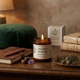 Candle labeled 'Ancient Incense' on a wooden surface with books and decorative items.