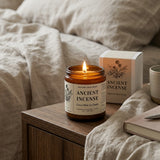 Ancient Incense candle on a wooden table with packaging and a cup in a cozy setting.