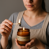 Person lighting an 'Ancient Incense' candle with a match.
