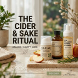 Three skincare products arranged on a stone tray with sliced apples and rosemary, under large text reading 'THE CIDER & SAKE RITUAL' and smaller text 'BALANCE. CLARIFY.