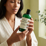Woman holding a bottle of 'Beer & Keratin' conditioner in a bathroom setting.