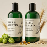 Two green bottles of 'Beer & Keratin' shampoo and conditioner with natural ingredients on a wooden surface.
