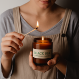 Person lighting a 'Black Sea' soy candle with a match.