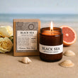 Black Sea artisan soy candle with packaging, flowers, and seashells on a sandy background