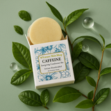 Caffeine soap bar in a box with green leaves and water droplets on a light green background