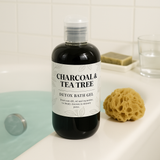 Bottle of Charcoal & Tea Tree Detox Bath Gel on a bathroom counter with a sponge and soap.