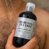 Bottle of Charcoal & Tea Tree Detox Bath Gel held by a person under a shower.