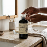 Person holding a bottle of activated charcoal wash on a bathroom counter.