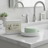 Green soap bar on a white dish with 'Clara' packaging in a bathroom setting.