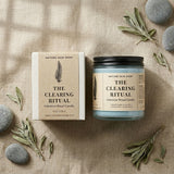 Nature Skin Shop 'The Clearing Ritual' candle and packaging on a textured surface with stones and herbs.