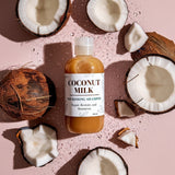 Bottle of coconut milk shampoo surrounded by coconuts on a pink background