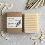 Coconut milk soap bar and packaging on a textured surface with coconut pieces.