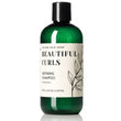 A bottle of Nature Skin Shop Beautiful Curls Defining Shampoo, featuring a dark green translucent bottle and a black cap, with a cream-colored label containing black text and botanical line art.