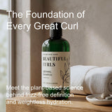 A green bottle of Beautiful Curls Defining Shampoo stands on a wooden surface in a softly lit bathroom-like setting, with a folded white towel and small dish in the background. Large overlaid text reads 'The Foundation of Every Great Curl' and 'Meet the plant-based science behind frizz-free definition and weightless hydration.