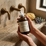 Person holding a bottle of Dead Sea Mud Ritual Wash in a bathroom setting.