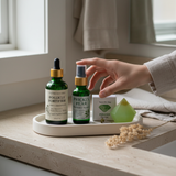 Bottles of skincare products on a tray with a hand reaching for one, in a bathroom setting.
