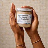 Hands holding a jar of Dead Sea Salt & Bio-Marine Foaming Polish against a neutral background