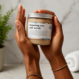 Hands holding a jar of foaming sea salt scrub with a neutral background
