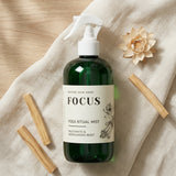 Green bottle labeled 'Focus Yoga Ritual Mist' with a white label on a beige fabric background.