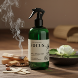 Green spray bottle labeled 'Focus' on a wooden surface with incense and lotus flower.