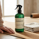 Green bottle labeled 'Harmony Yoga Ritual Mist' on a wooden surface with a person's hand and folded towel in the background.