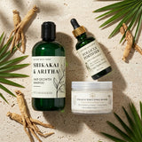 Three hair care products on a textured surface with green leaves and roots.