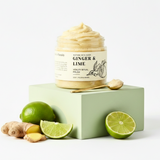 Jar of 'Ginger & Lime' product on a green block with ginger and lime slices on a white background