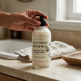 Hand holding a bottle of 'Glycolic Renewal' lotion on a bathroom counter.