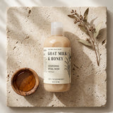 Bottle of Goat Milk & Honey wash on a stone surface with a wooden bowl and leaves.