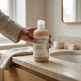 Person holding a bottle of 'Goat Milk & Honey' wash on a bathroom counter.