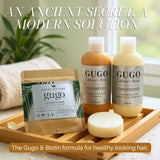 Gugo shampoo, conditioner, and shampoo bar on a wooden tray with a blurred indoor background.