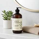 Brown bottle labeled 'Gugo & Caffeine' on a bathroom counter with a plant and towel in the background.