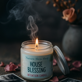 Candle labeled 'House Blessing' from Nature Skin Shop with smoke and flowers in the background