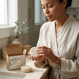 Woman in a bathrobe holding a bar of soap next to a Keratin product box in a bathroom setting.