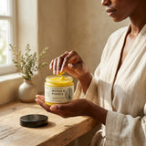 Person applying mango and papaya cream from a jar on a wooden table.