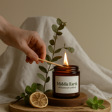 Hand lighting a 'Middle Earth' artisan soy candle with a wooden coaster and greenery.