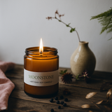 Moonstone artisan soy candle in a glass jar with a label, surrounded by decorative elements on a wooden surface.